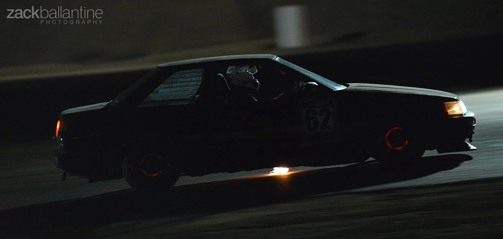 Night motorsport — a Toyota AE86 with glowing brakes and an exhaust flame at the Streets of Willow