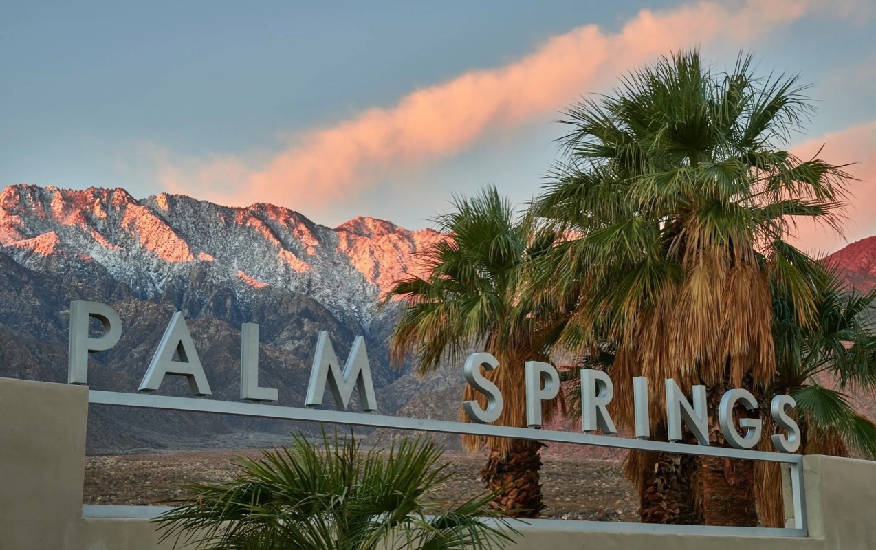 The Palm Springs city sign at sunrise beneath snow-dusted mountains